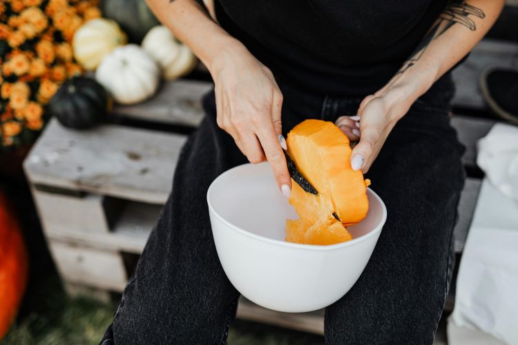 A pet owner chopping up a small pumpkin in a bowl to prepare it for pet-safe consumption.