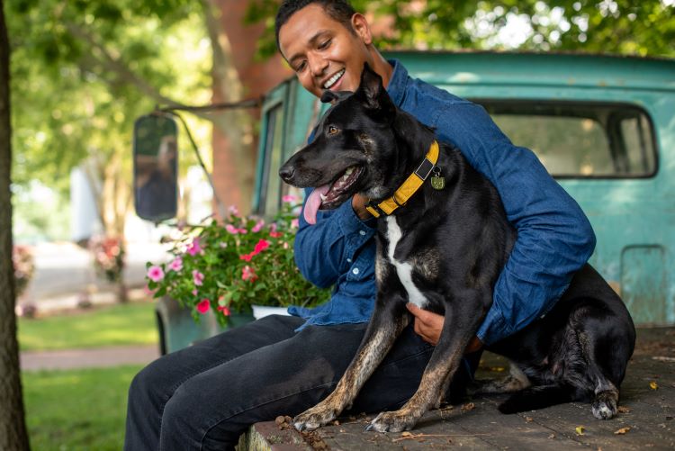 Pet owner sitting outdoors on a truck bed with his black dog protected by Trupanion pet insurance.