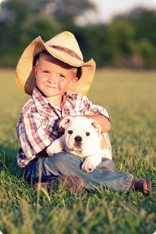 A boy wearing a cowboy hat with a puppy in his lap