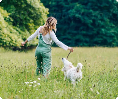 A female pet owner with affordable pet insurance playing with their white dog in a green field.