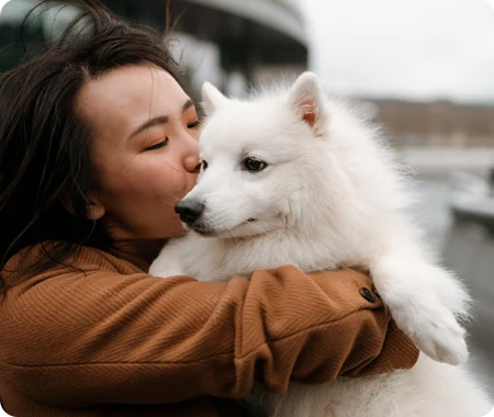 A female pet owner learning about Trupanion pet insurance cost kissing their white dog outdoors.