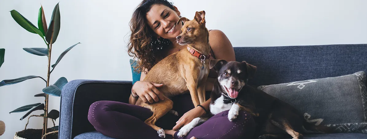 Woman on the couch holding two dogs in her lap.