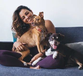 Woman on the couch holding two dogs in her lap.